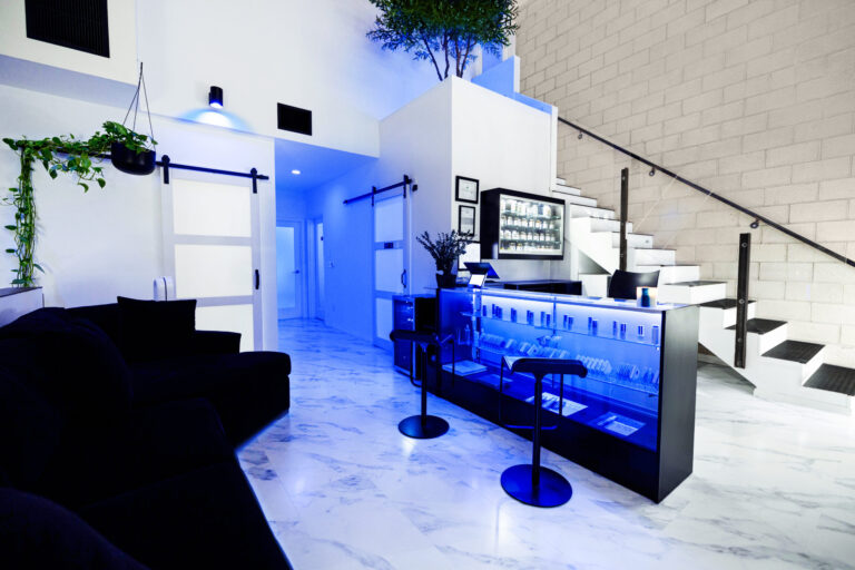 Modern, stylish lounge in Los Angeles with marble floors, blue-lit counter, black couch, and Hollywood glamour.