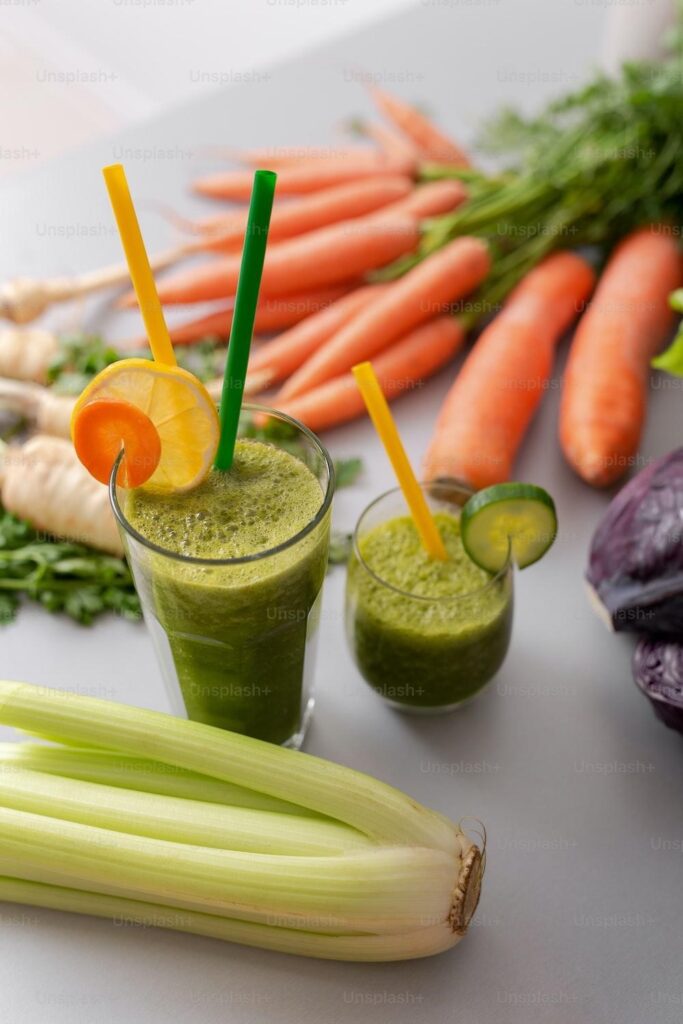 Two glasses of green smoothie with straws, like a scene from Hollywood, surrounded by fresh veggies in Los Angeles.