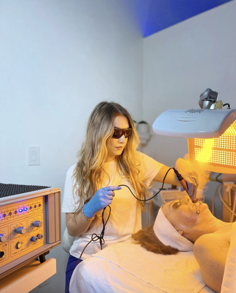 A woman in sunglasses performs the best facial on a client under a yellow light in Los Angeles.
