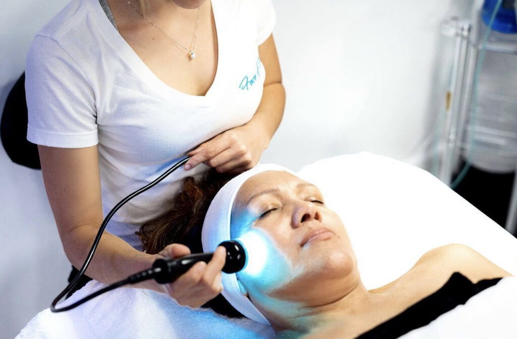 A woman enjoys a facial with a blue light device from a skincare professional in a Hollywood clinic.
