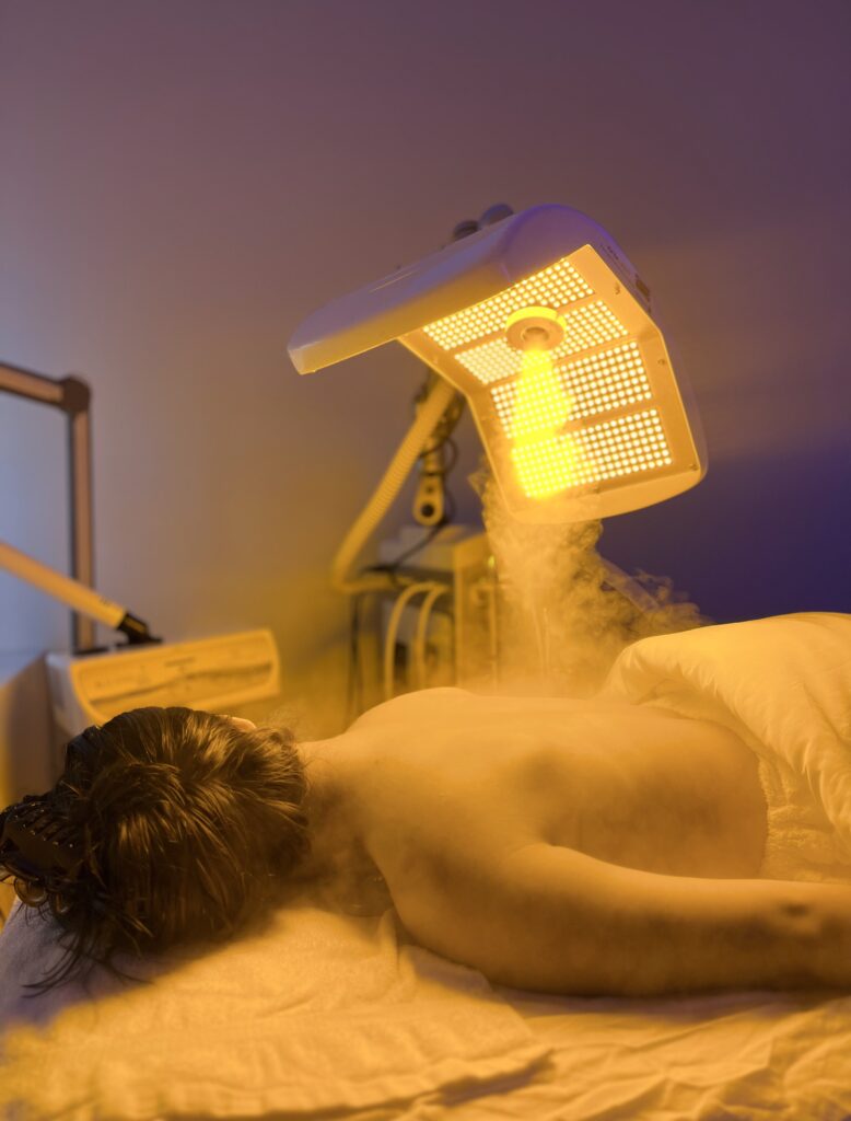 Relax beneath a yellow LED light panel with soothing steam during the best facial in Los Angeles.